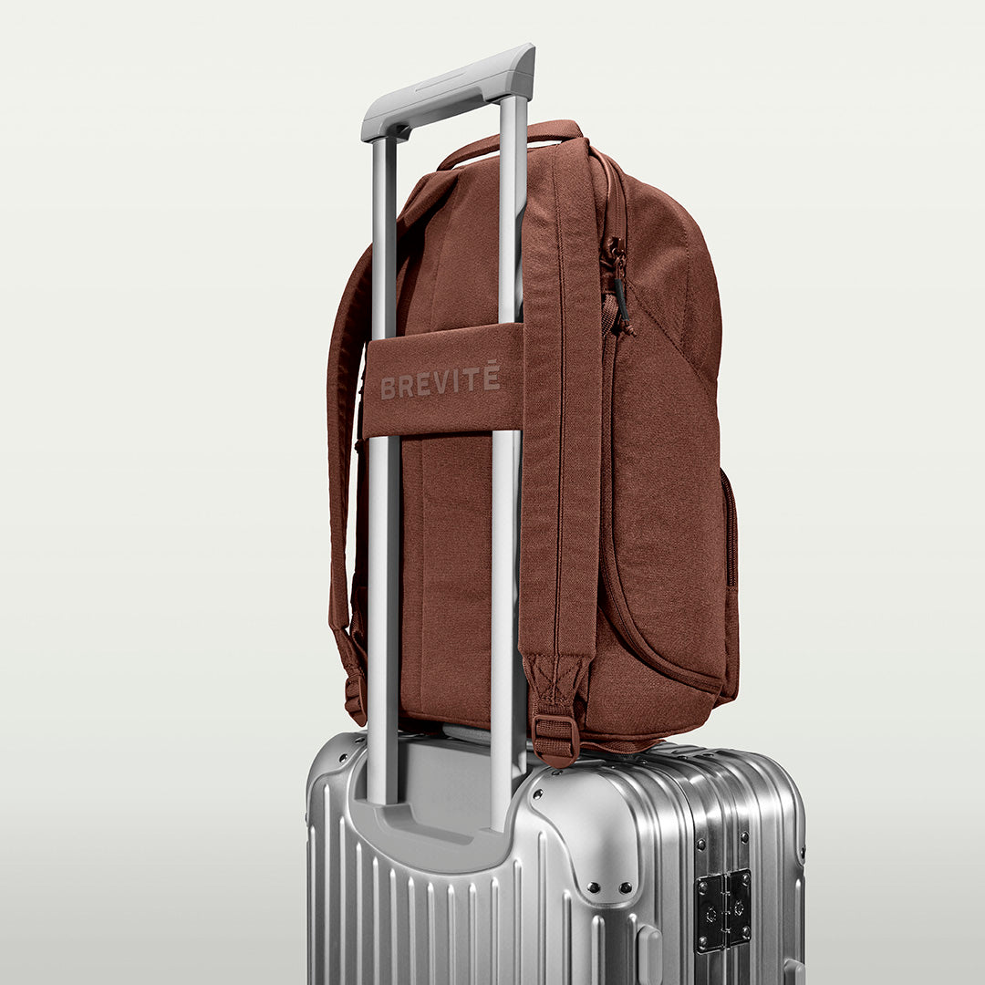 The Brevitē Backpack in Burnt Brown, luggage strap over a suitcase handle