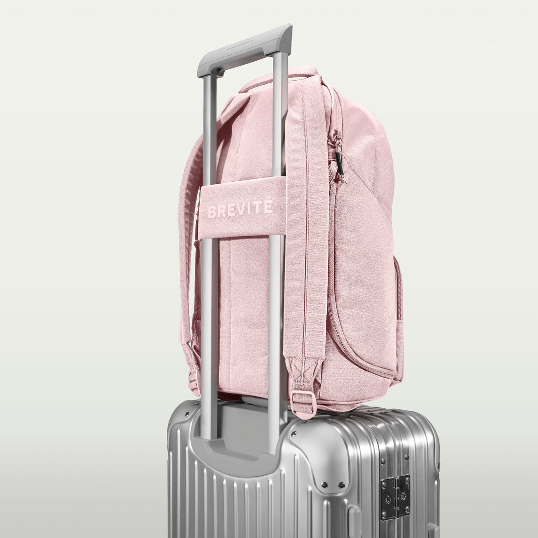 The Brevitē Backpack in Blush Pink, luggage strap over a suitcase handle