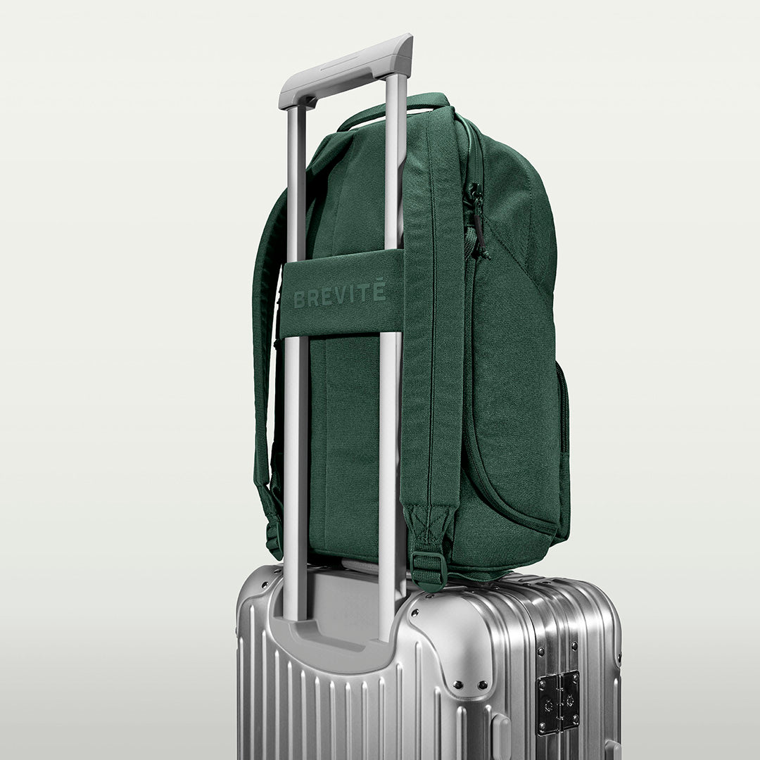 The Brevitē Backpack in Jade Green, luggage strap over a suitcase handle