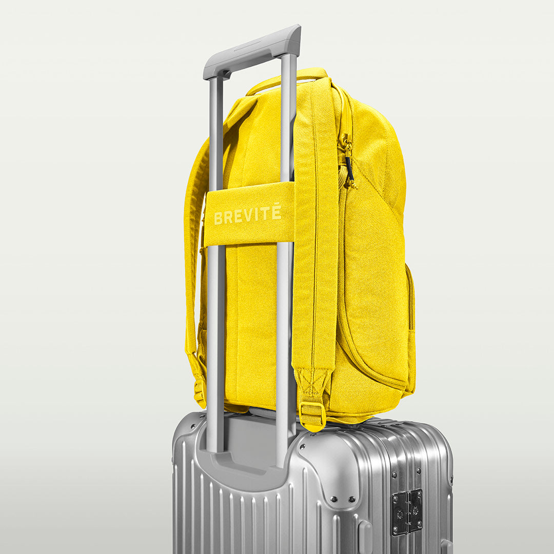 The Brevitē Backpack in Lemon Yellow, luggage strap over a suitcase handle