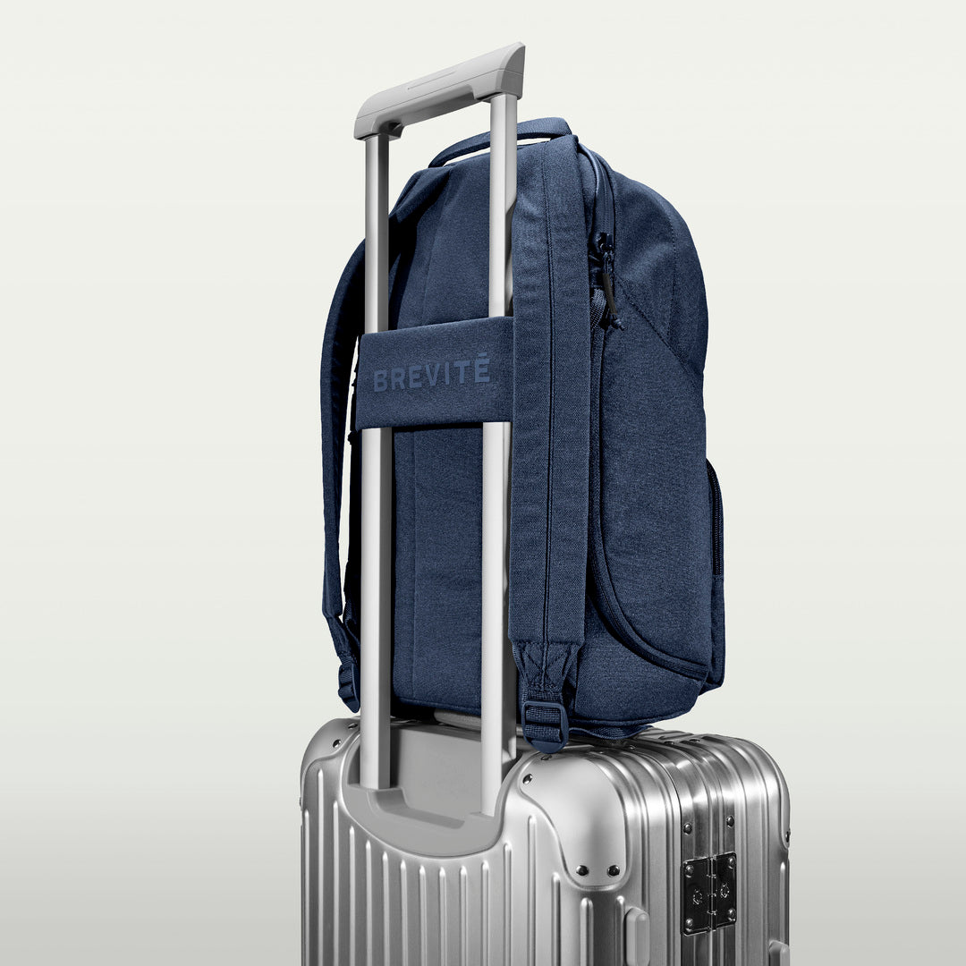 The Brevitē Backpack in Moonlit Blue, luggage strap over a suitcase handle