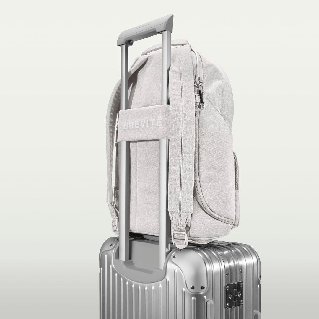 The Brevitē Backpack in Nimbus Gray, luggage strap over a suitcase handle