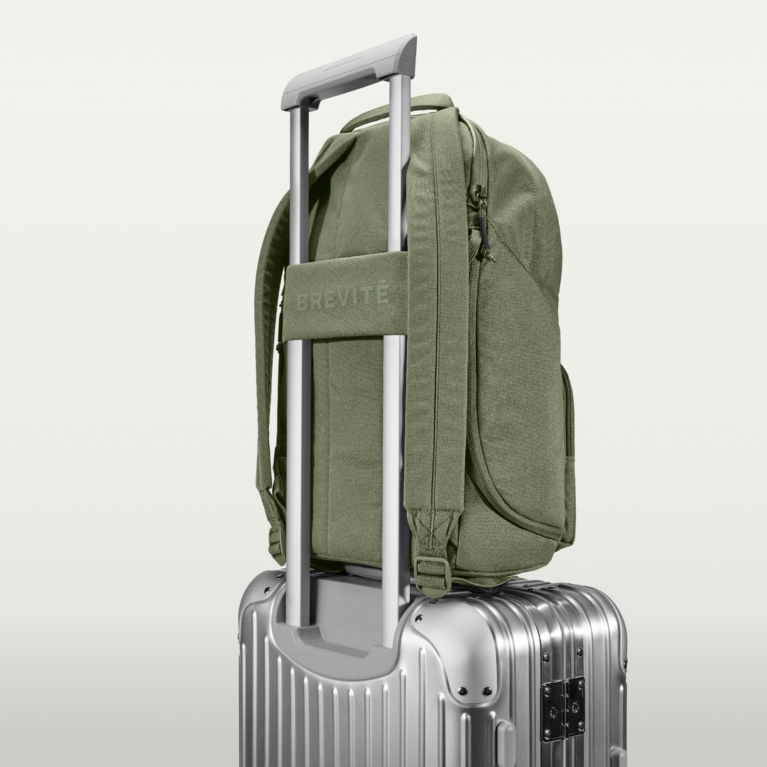 The Brevitē Backpack in Pine Green, luggage strap over a suitcase handle