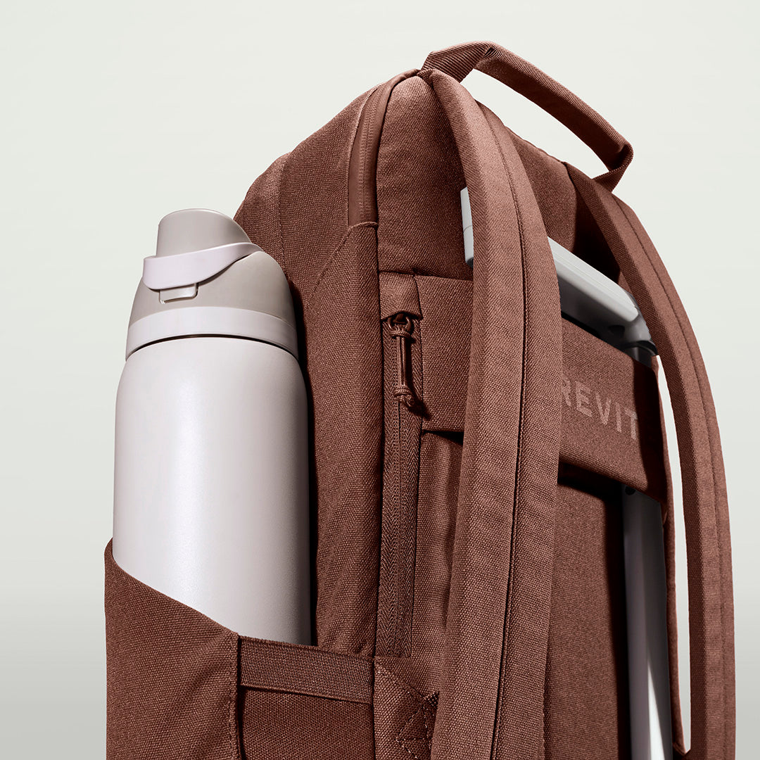 The Brevitē Backpack in Burnt Brown, large water bottle in the side pocket
