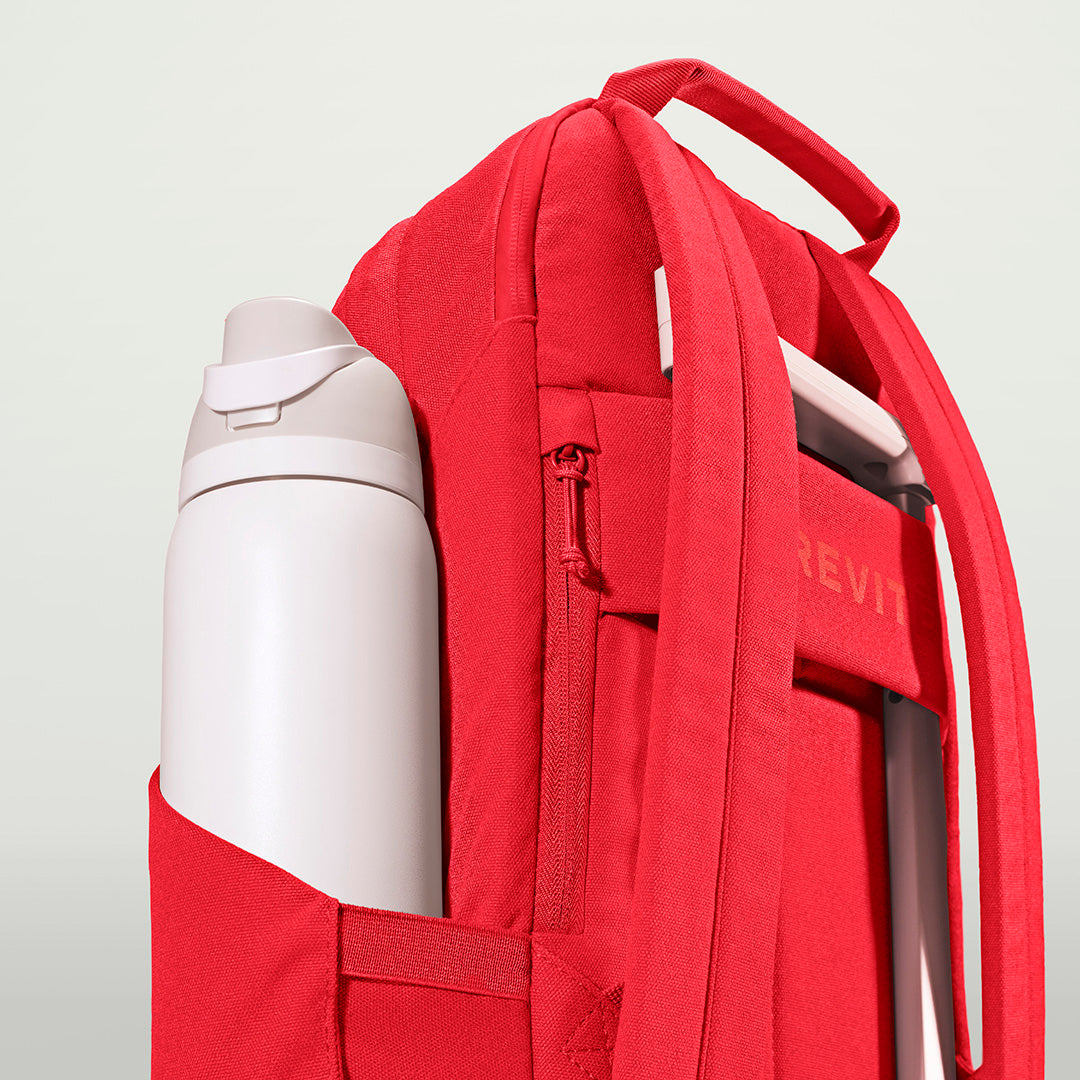The Brevitē Backpack in Poppy Red, large water bottle in the side pocket
