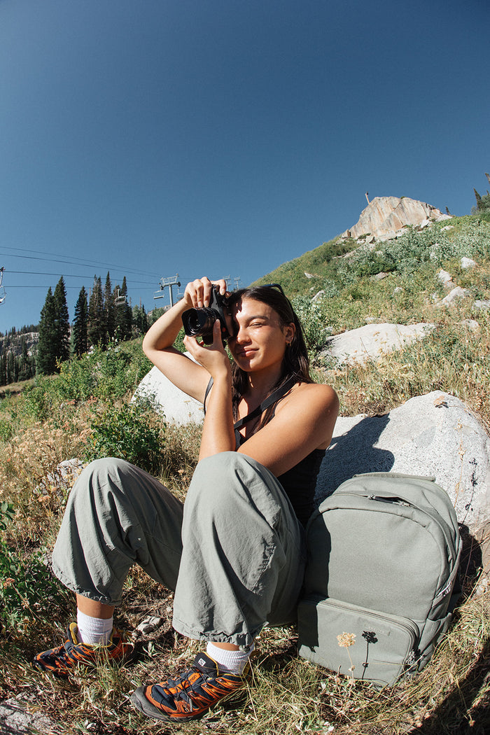 A photographer on a mountain hillside in Big Cottonwood Canyon with her backpack beside her