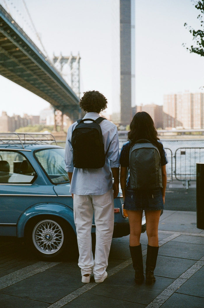 Two friends wearing Brevitē backpacks under the Manhattan Bridge in Dumbo