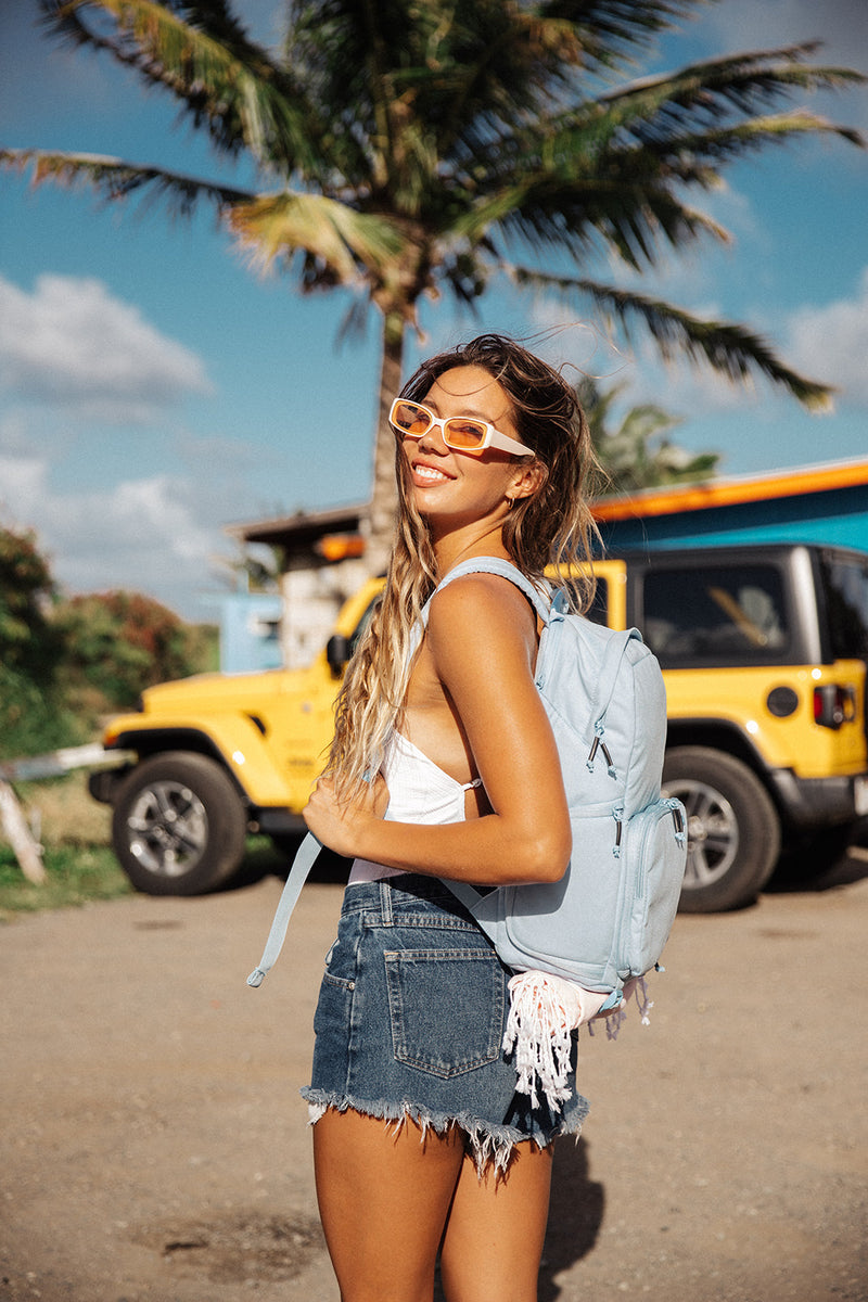 Woman with a Misty Blue Brevitē backpack in front of a yellow Jeep and palm tree in Hawaii