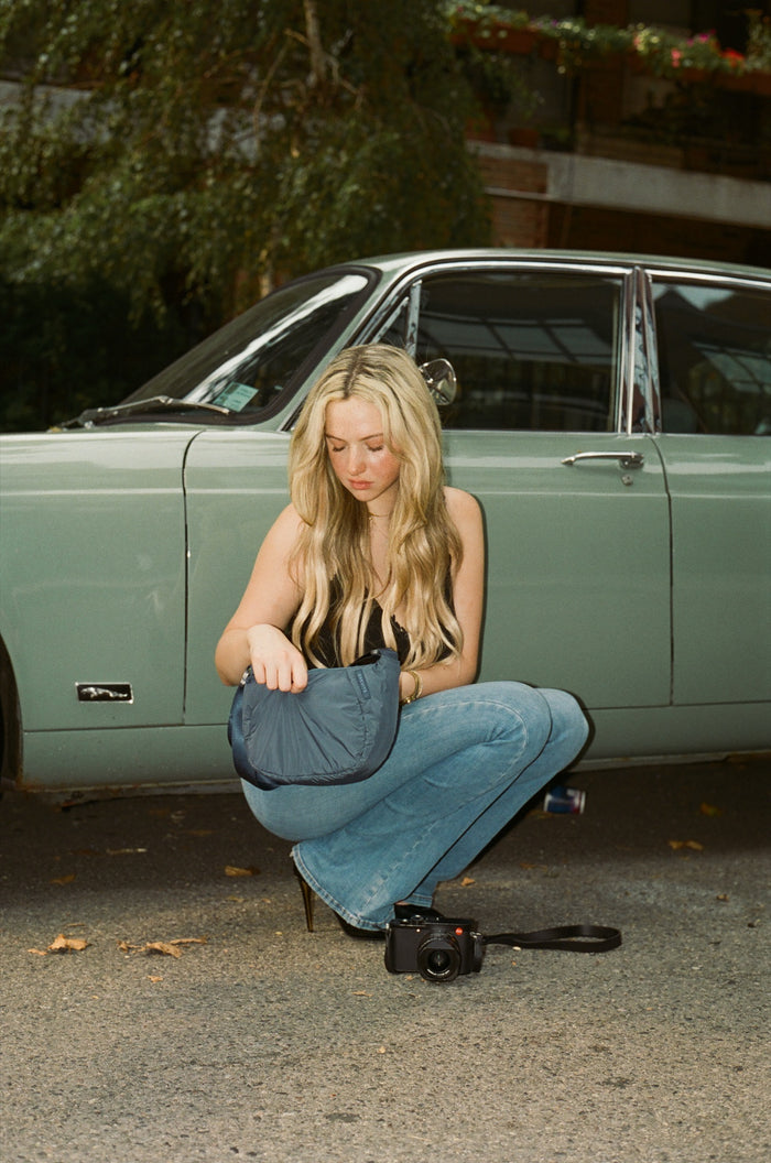 A woman crouching by a mint green vintage car with her camera at her feet