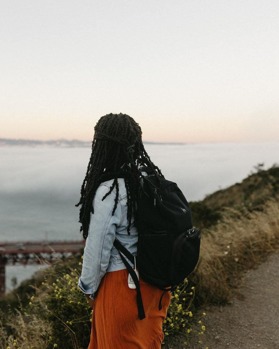 A woman in a denim jacket with a black Brevitē backpack looking over the Golden Gate Bridge at dusk