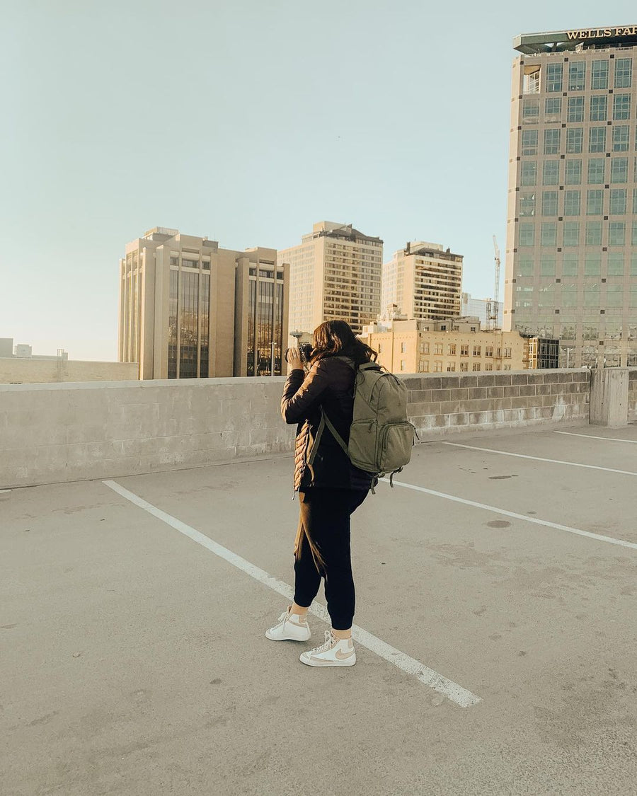 A photographer with a green Brevitē backpack shooting the city skyline from a rooftop parking deck