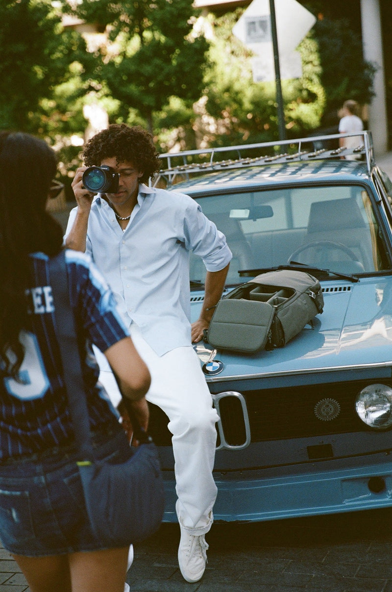 A photographer raising a camera to their eye beside a vintage blue BMW